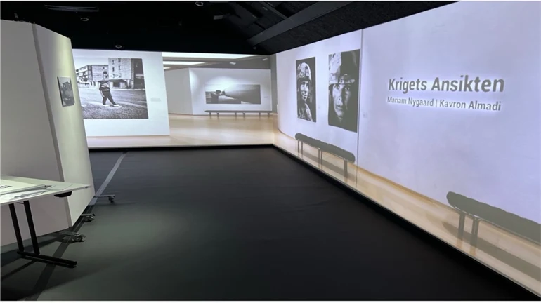 Exhibition space with projected photos and the text “Krigets Ansikten” with two names.