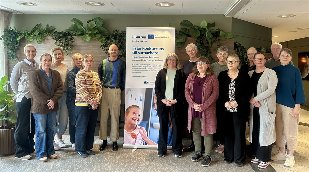 Femton personer står framför en grågrön vägg.