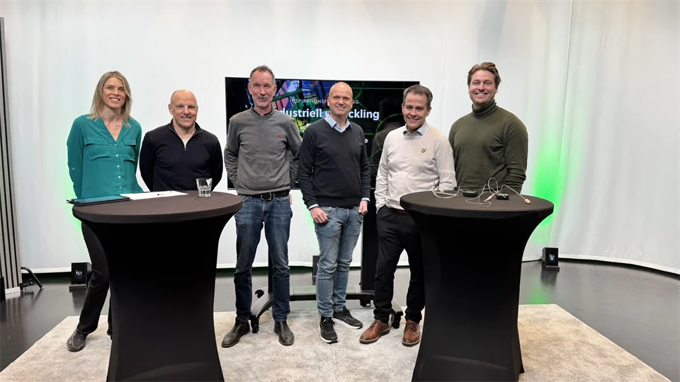 6 personer står bakom två stå bord och ler mot kameran