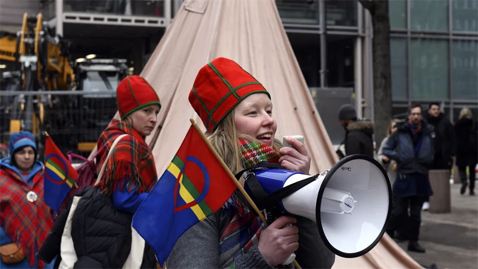 Woman holding a Saami flag and speaking in a megaphone.