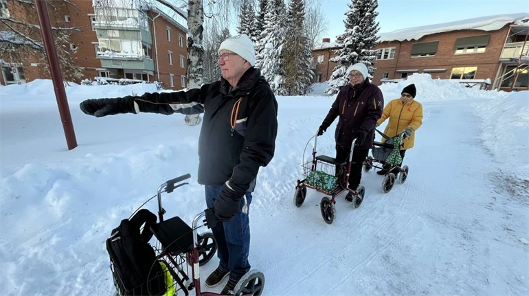 Tre äldre iklädda varma vinterkläder är ute och promenerar med sina rollatorer.