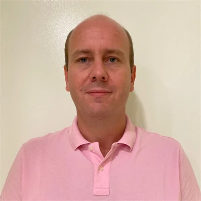 Man i rosa piketröja står mot en beige vägg.