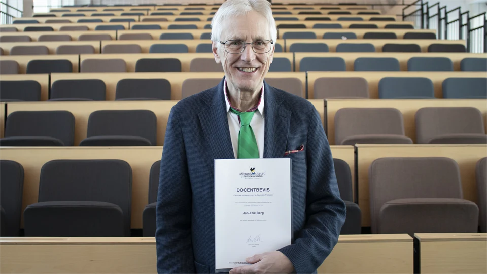 Man in grey jacket and green tie shows a docent certificate in front of an empty hall