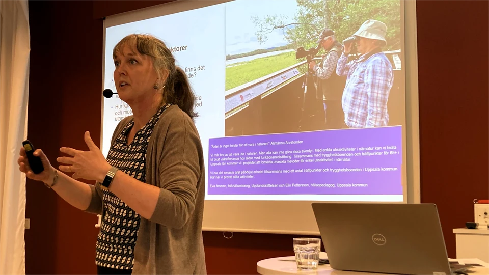 En kvinna står framför en skärm med en presentation och gestikulerar med händerna