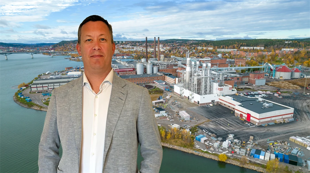 En man står framför en bild av ett fabriksområde.