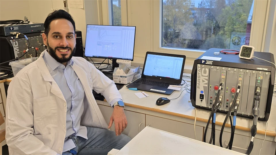 En man i en vit laboratorierock sitter vid datorer och laboratorieutrustning. 