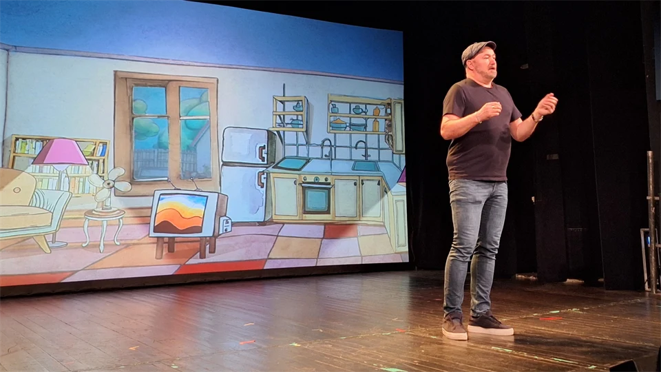 En man med svart t-shirt står på en scen och pratar