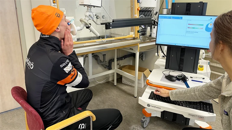Young man blows into a mouthpiece, test leader monitors on monitor.
