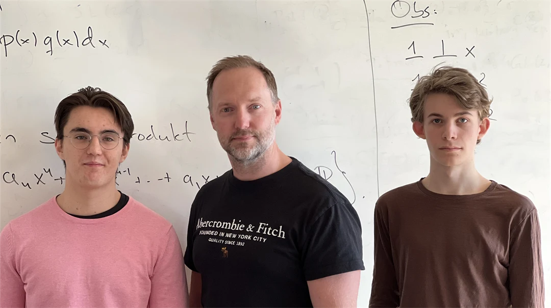 Two younger men and a middle-aged man stand in front of a whiteboard.