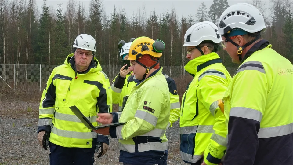 En grupp män i varselkläder står tillsammans och tittar på en bärbar dator. 