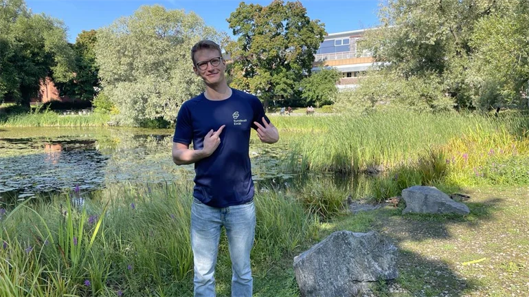 En man med blå tröja står vid vid en damm