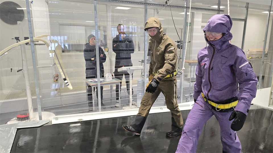 Två personer i färglada kläder går i en glastunnel medan två personer tittar på.