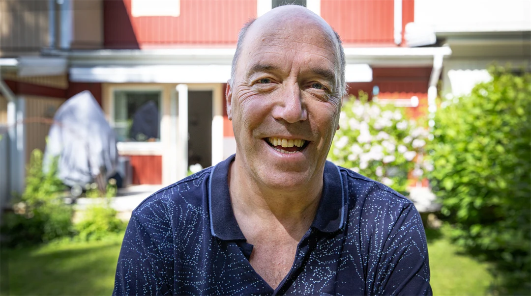 En man står med ryggen mot ett hus med lummig trädgård.