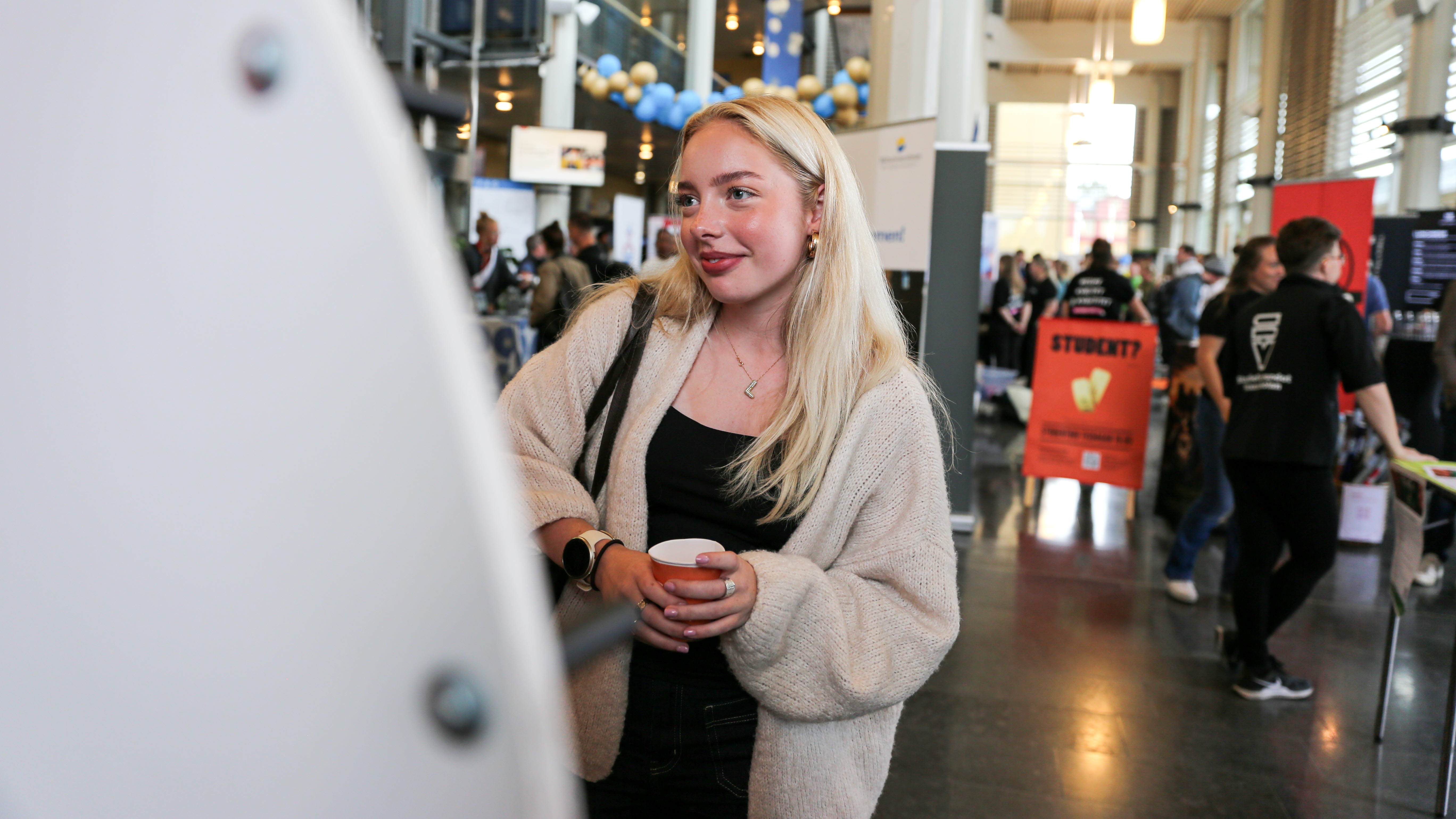 En kvinna i blont hår står framför ett lottohjul.