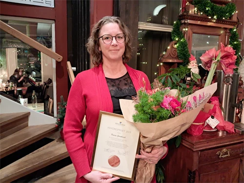 Kvinna i röd kavaj med diplom och blombukett i famnen