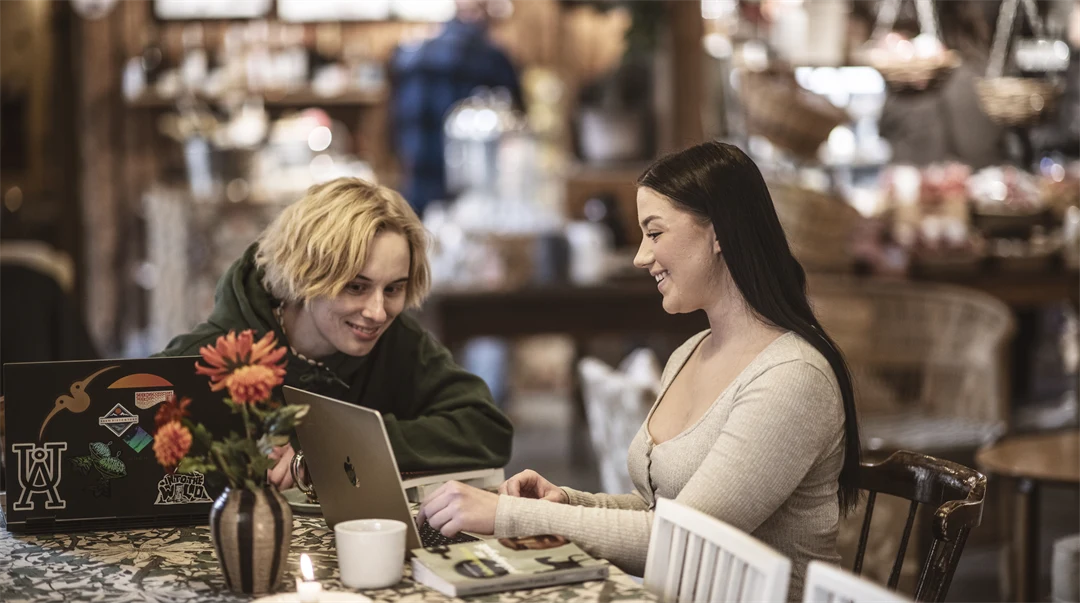 Två kvinnor sitter vid ett bord, tittar på en dator.