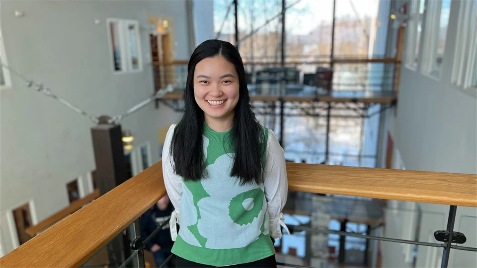 En kvinna står i en ljusgård och tittar in i kameran och ler. 