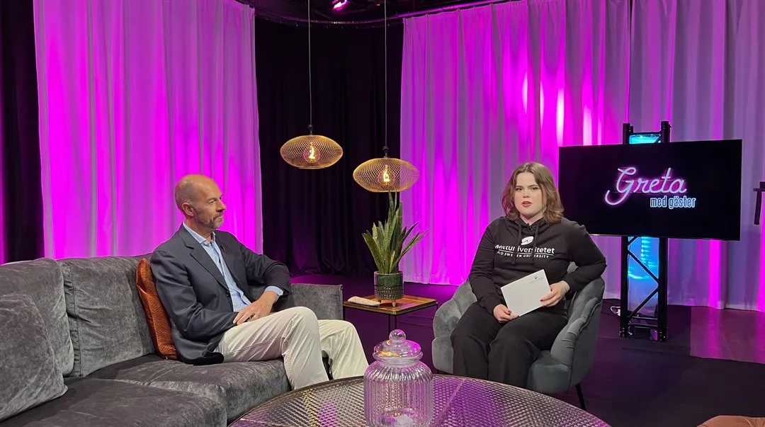 Två personer sitter i en studio, en i en soffa och en i en fåtölj.