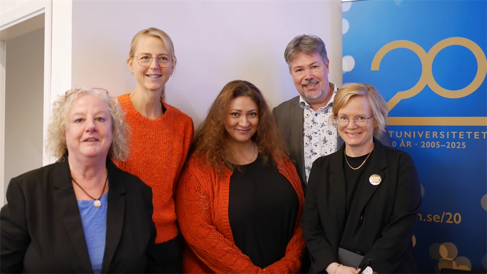Fyra kvinnor och en man står framför en skylt med texten Mittuniversitetet 20 år. De ser glada ut.