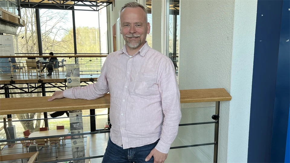 A man in a light shirt stands in a light yard.
