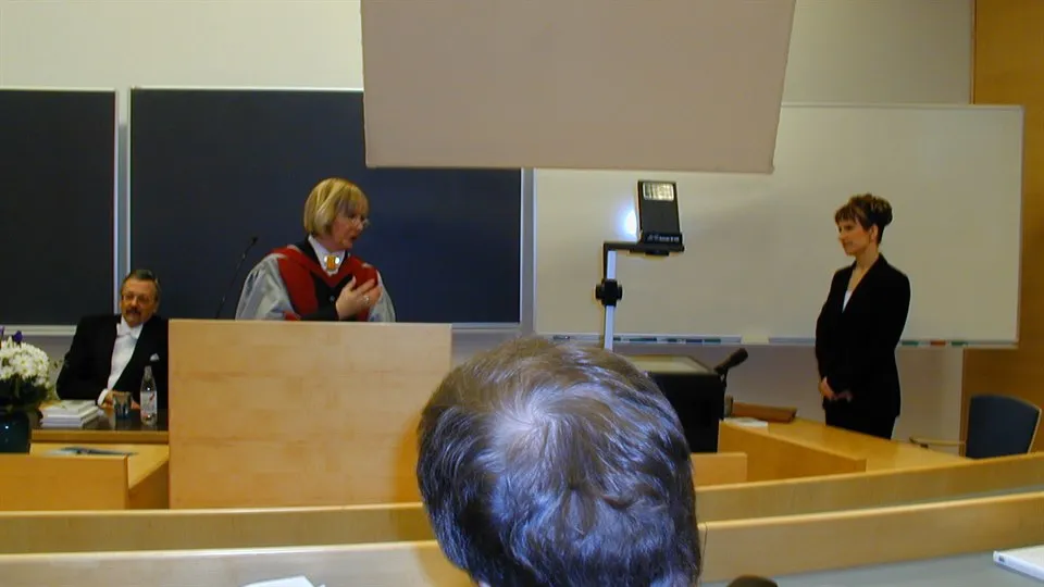 Kvinna står vid podium i föreläsningssal vid en disputation