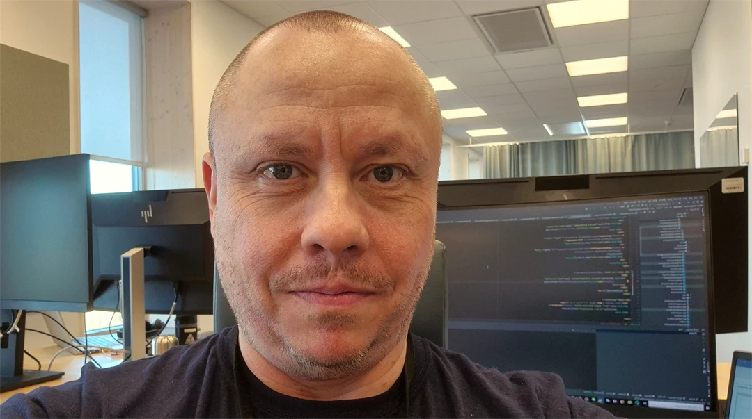 En man sitter i ett kontorslandskap med en datorskärm bakom sig.