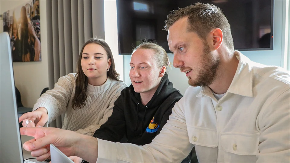  Three people are sitting next to each other and looking at a computer screen.
