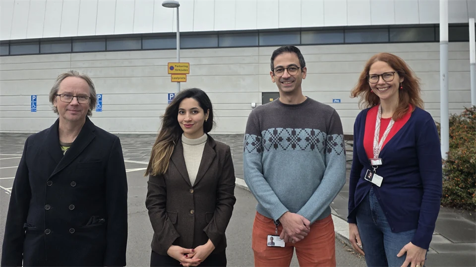 Fyra personer, två män och två kvinnor, står utomhus framför en stor byggnad. 