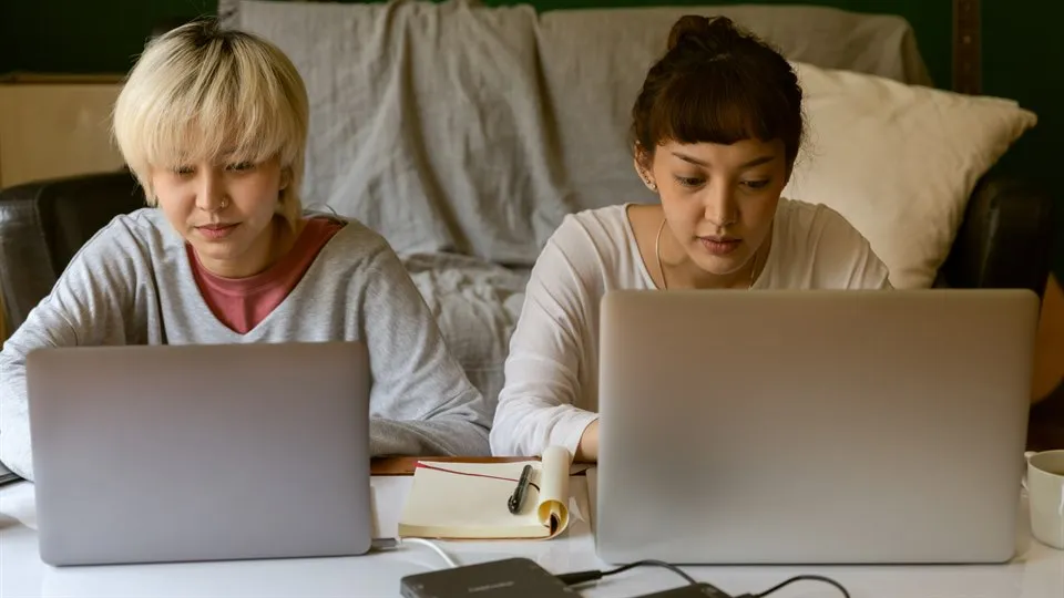 Two friends sitting with their laptops next to eachother