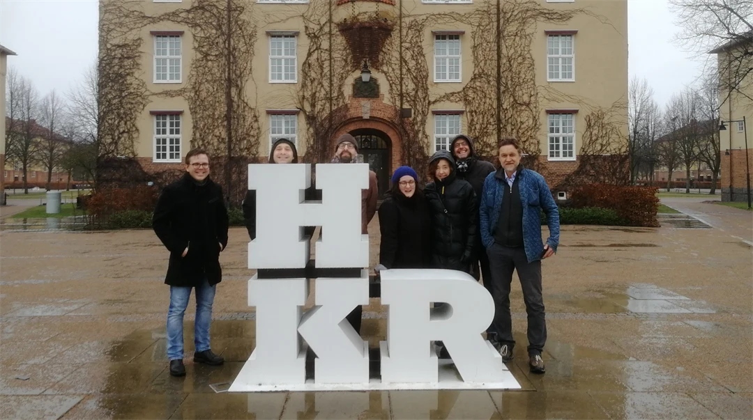 En grupp människor står bakom ett konstverk föreställande bokstäverna HKR med en stor byggnad i bakgrunden. 