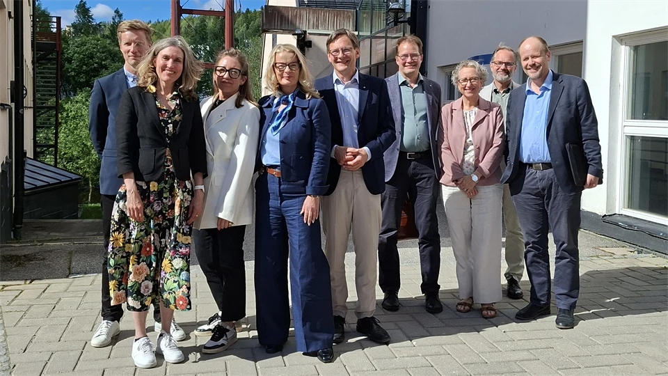 Gruppbild med nio personer ståendes utomhus i solen.