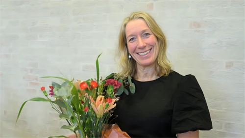 Kvinnlig forskare står i en lärosal med en blombukett i famnen