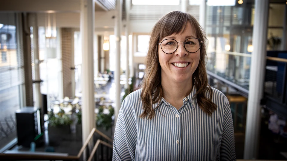 Kvinna i randig skjorta står i stor hall.