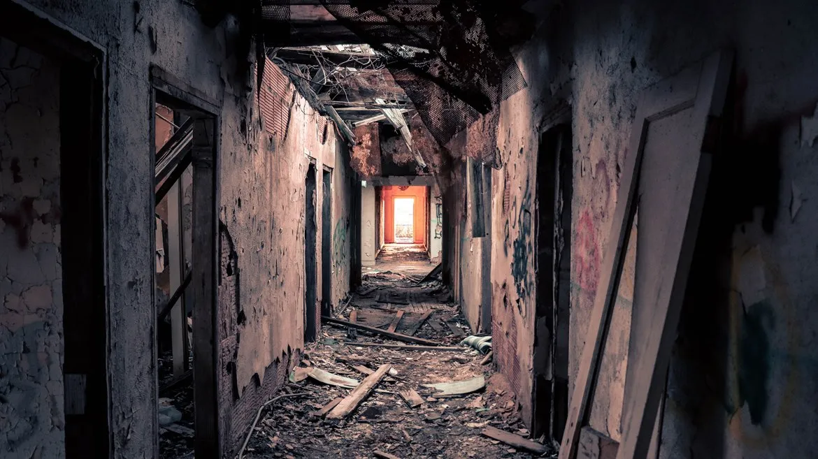Korridor i ett övergivet hus. Tak och väggar är trasiga och det ligger brädor och skräp på golvet.