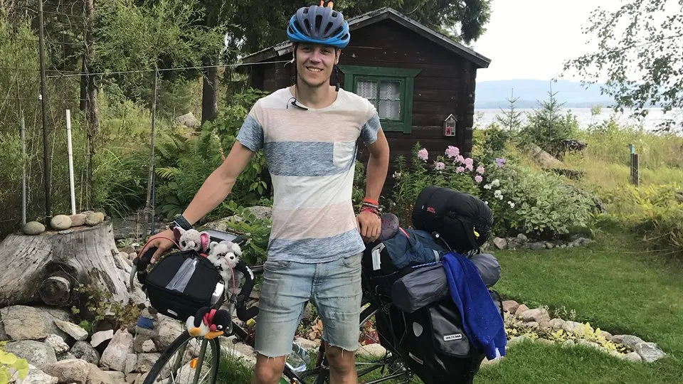 Ung man står vid fullpackad cykel.