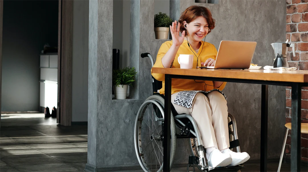 Kvinna i orange top sitter i rullstol vid ett bord.