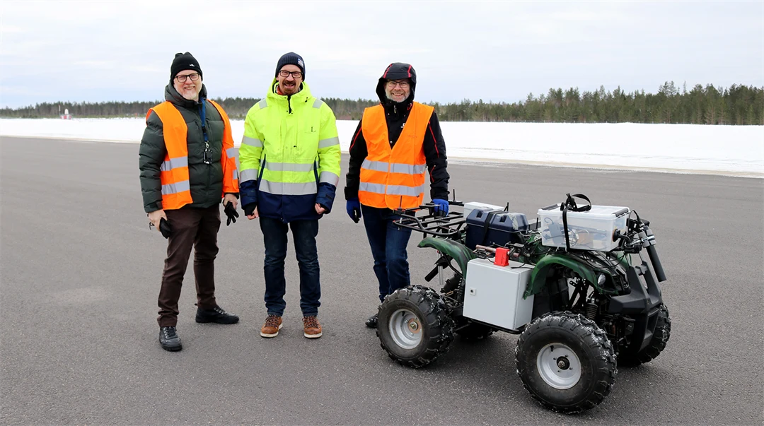 Tre forskare i varselkläder står vid en autonom fyrhjuling på en landningsbana