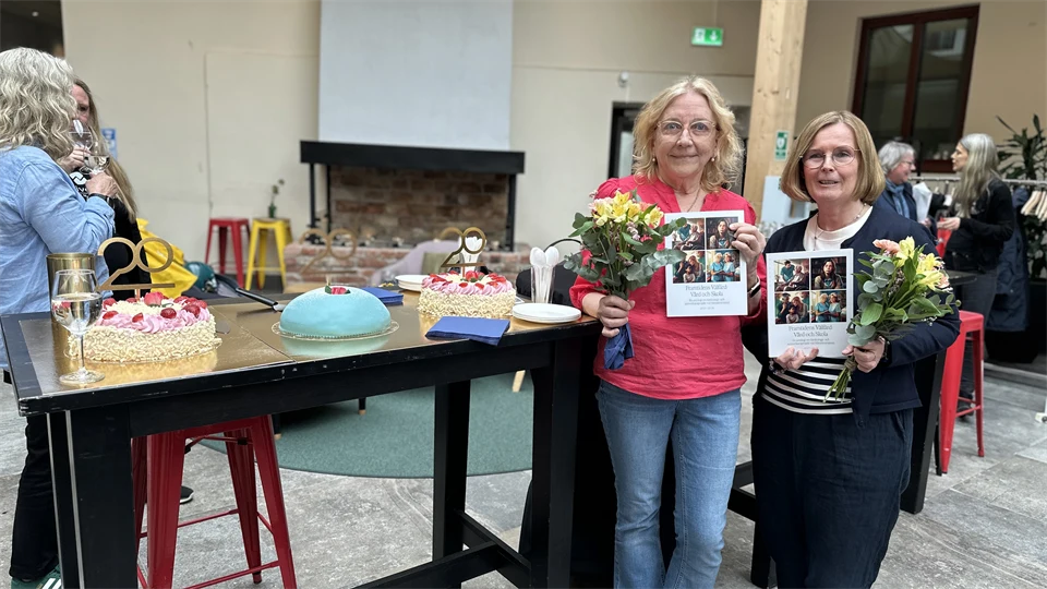 Två blonda kvinnor håller upp en bok och blommor