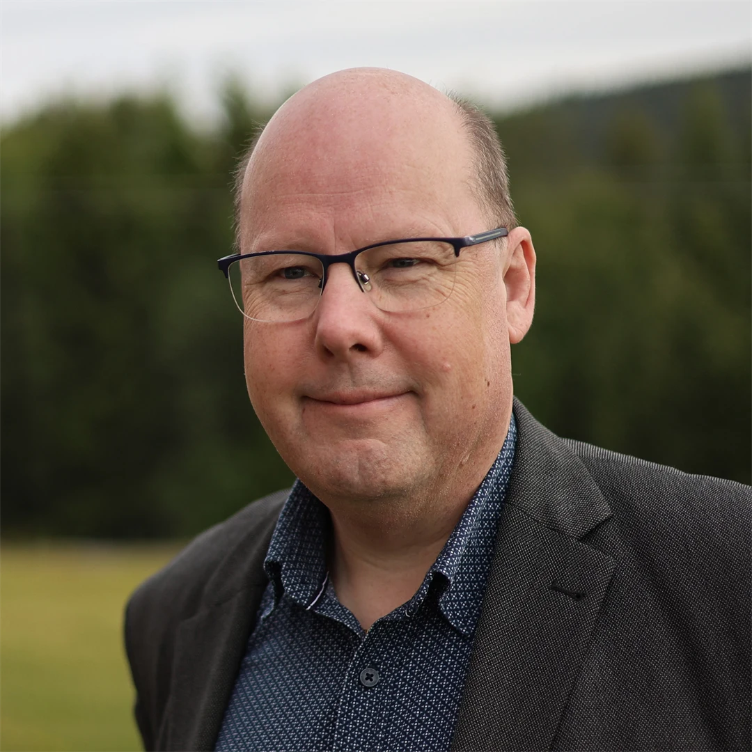 En man med glasögon, klädd i kavaj, tittar in i kameran.