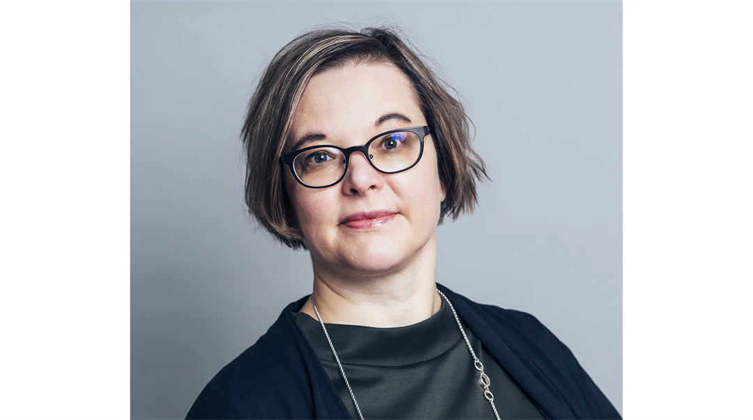 A woman with dark hair, glasses, wearing a black top.