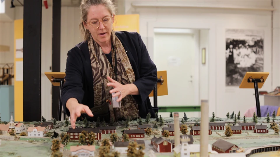 Kvinna står bredvid och visar en modell av en by i miniatyr 