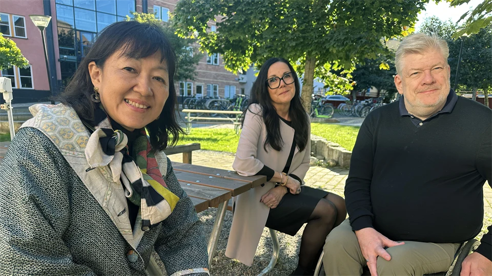 Två kvinnor och en man sitter vid ett utebord