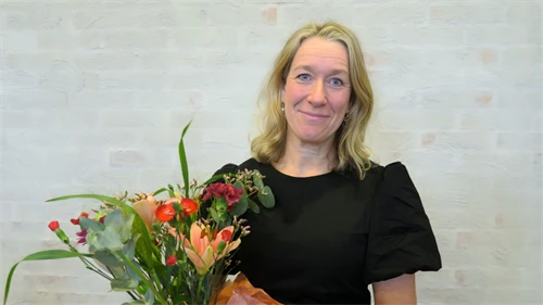 Kvinnlig forskare står i en lärosal med en blombukett i famnen