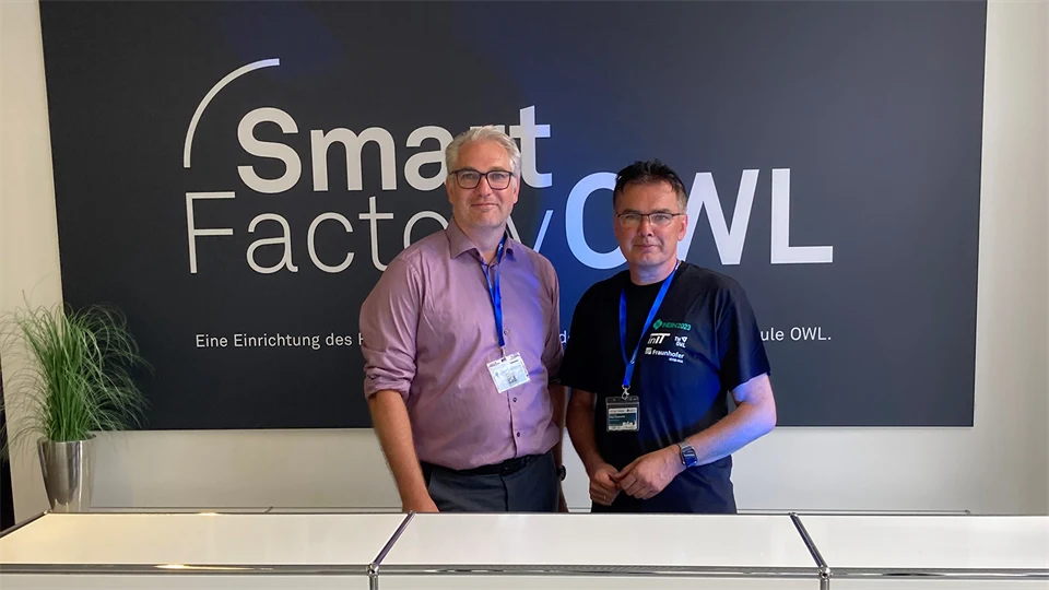 Två män står och ler mot kameran med en skylt bakom där det står Smart Factory OWL 