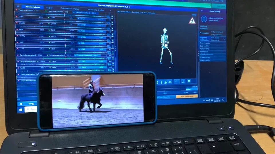 En mobil som står framför skärmen på en bärbar dator visar en film på en islandshäst med ryttare. Datorskärmen visar en rörlig tredimentionell bild av ryttaren som skapas av sensorer som ryttaren bär på kroppen.