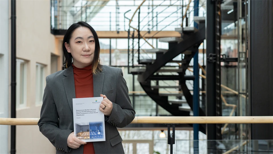 En kvinna inomhus håller i en avhandling med båda händer och ler mot kameran