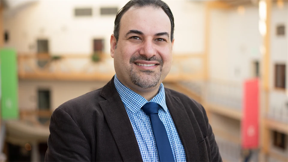 A man with dark hair, black jacket, light blue shirt and dark blue tie.