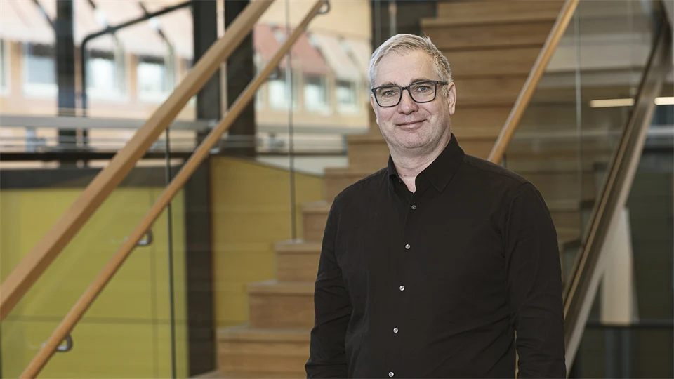 Man med glasögon i svart skjorta framför en trappa