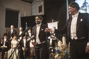 Två finklädda personer med lagerkransar står på en scen.