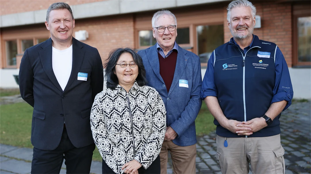 Gruppbild med leende personer framför tegelbyggnad